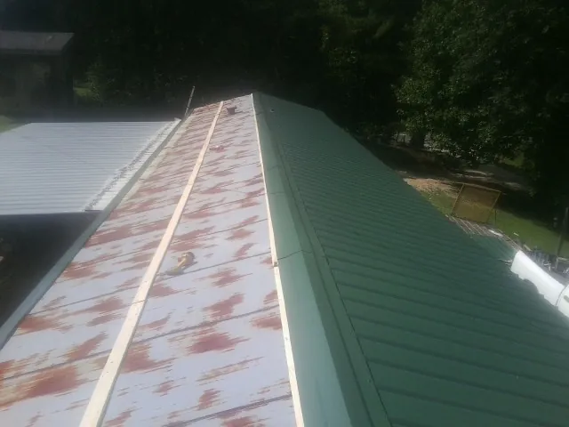 Old rusted panels beside newly installed green metal roofing — Wind Damage Roof Repair by Roofing Brothers in Houma
