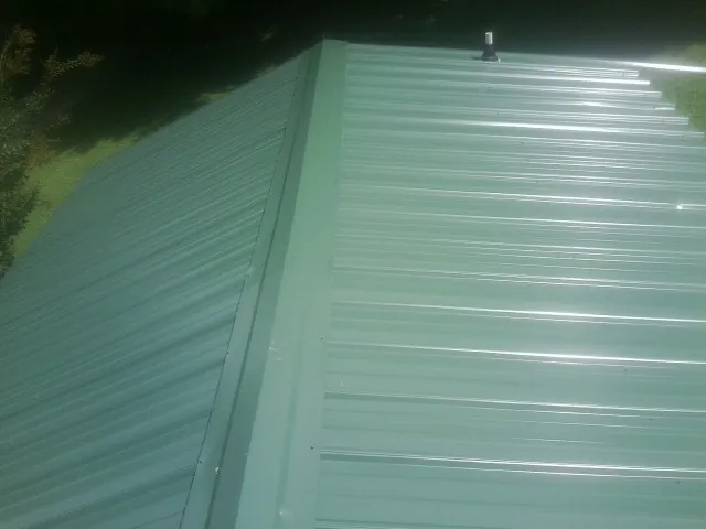 New green metal panels meeting at the ridge of a roof — Flat Roof Repair work by our crew in Houma