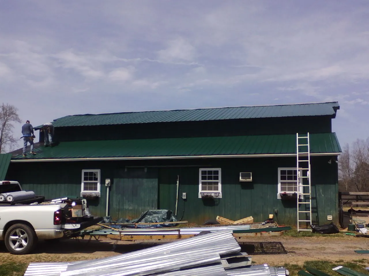 Crew installing green metal roofing on a large green barn in Houma
