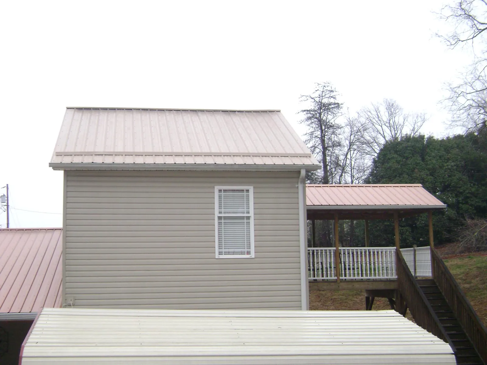Tan metal roofs on a two story addition and attached porch, from a Roof Replacement job in Houma